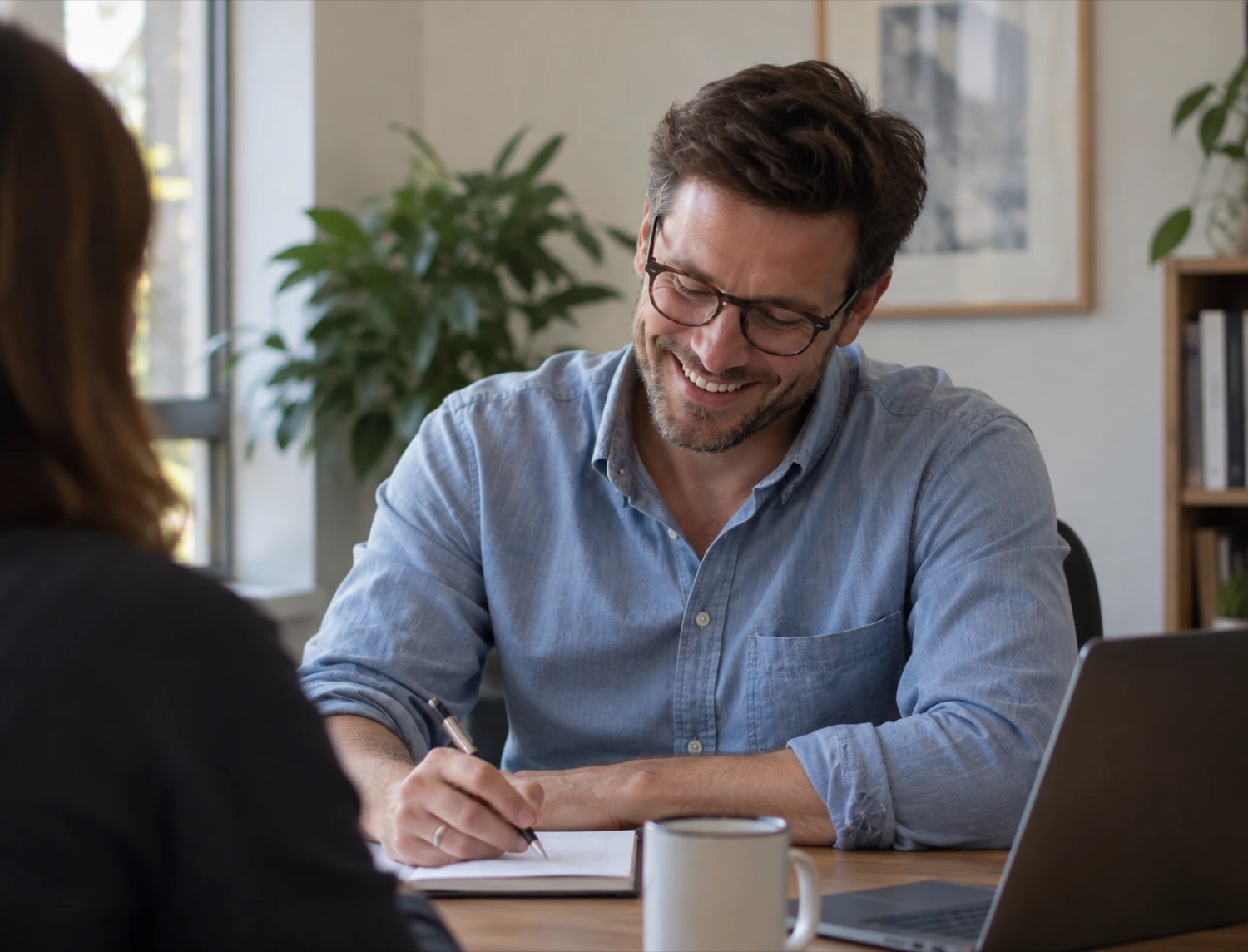A smiling man taking notes during a relaxed one-to-one conversation