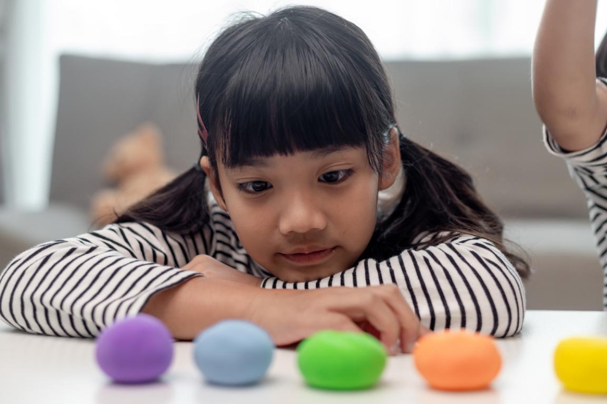 A child resting their head on their arms, looking at small pieces of modelling clay